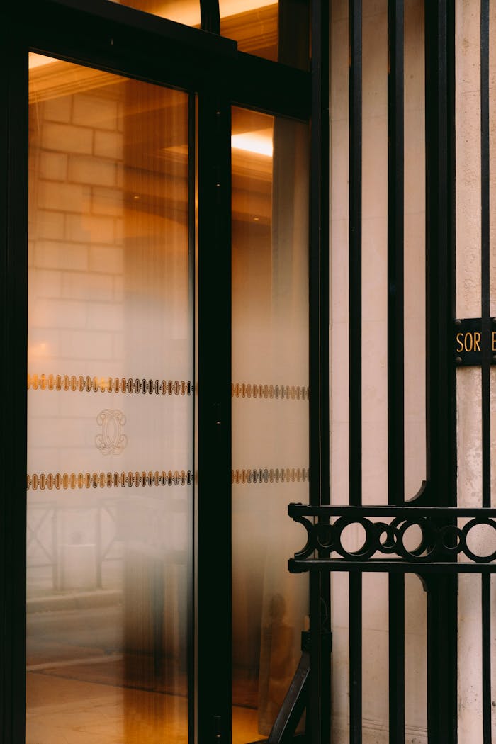 A stylish glass door with steel bars features reflections and warm lighting, creating an inviting entrance.