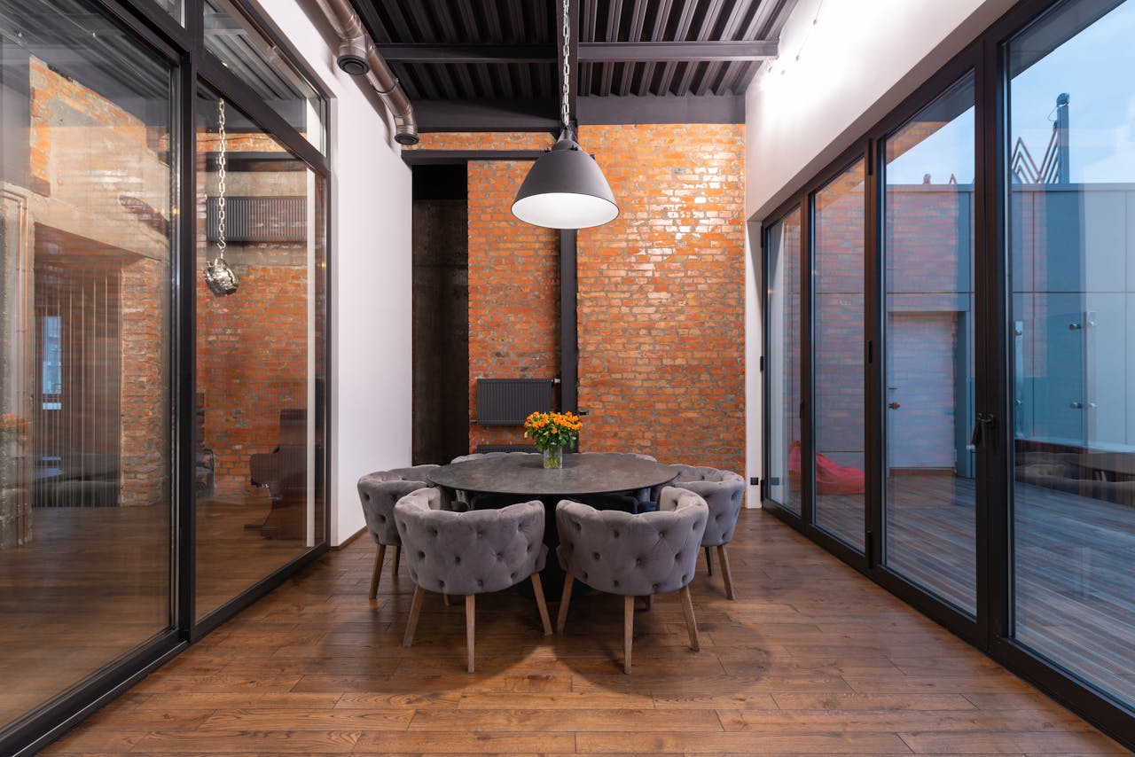 Dark round table with bouquet of flowers and comfortable armchairs placed in spacious room with glass walls in cloudy day